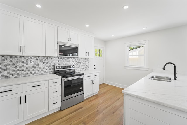 kitchen featuring a sink, light wood finished floors, stainless steel appliances, white cabinetry, and tasteful backsplash