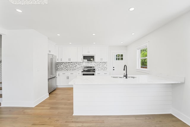 kitchen with white cabinets, appliances with stainless steel finishes, a sink, a peninsula, and light wood-type flooring