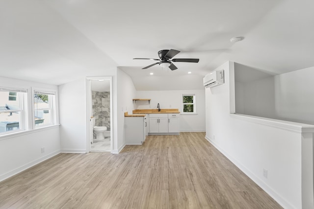 unfurnished living room with a wall unit AC, a ceiling fan, a sink, light wood-style floors, and a wealth of natural light