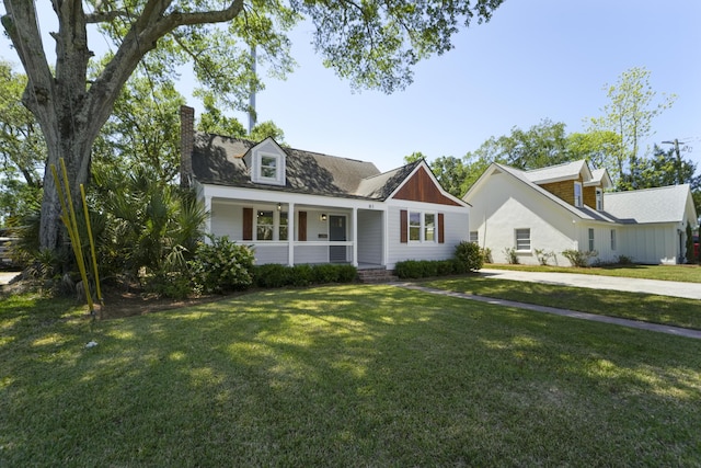 cape cod-style house featuring a chimney, covered porch, and a front yard