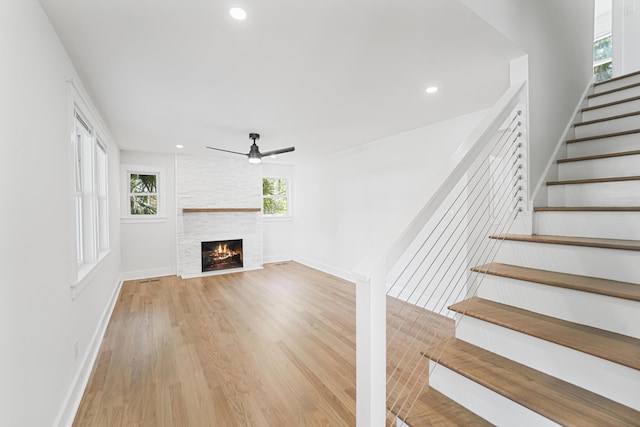 unfurnished living room with a large fireplace, ceiling fan, light wood finished floors, and a wealth of natural light