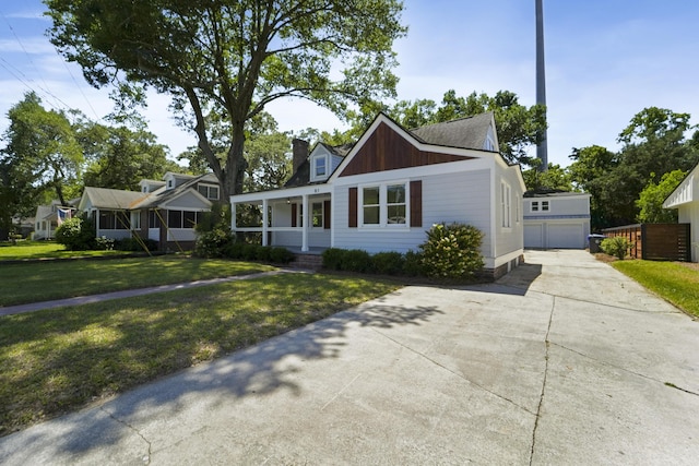 view of front of home with covered porch, a chimney, an outbuilding, a detached garage, and a front lawn