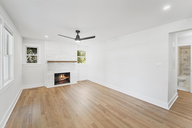 unfurnished living room with light wood-style floors, a stone fireplace, a ceiling fan, baseboards, and visible vents