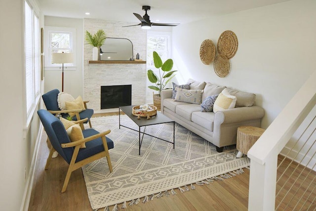living area featuring a ceiling fan, wood finished floors, a healthy amount of sunlight, and a fireplace