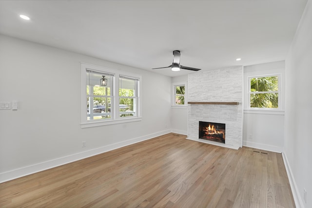unfurnished living room with a fireplace, light wood-style flooring, a ceiling fan, baseboards, and visible vents