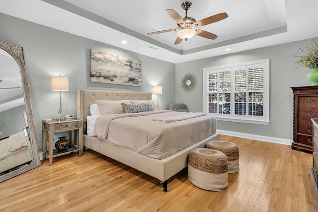 bedroom with a raised ceiling, ceiling fan, and light hardwood / wood-style floors