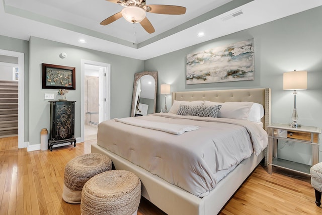 bedroom featuring ceiling fan, hardwood / wood-style floors, ensuite bath, and a tray ceiling