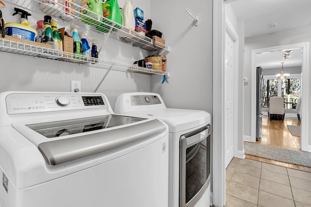 laundry area with light tile patterned flooring, washer and clothes dryer, and a chandelier