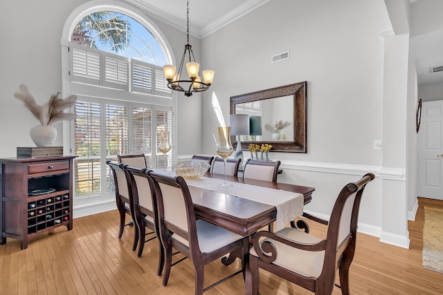 dining room with a notable chandelier, crown molding, light hardwood / wood-style floors, and a high ceiling