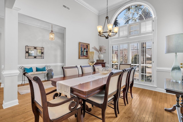 dining area with decorative columns, crown molding, a notable chandelier, light hardwood / wood-style floors, and a high ceiling