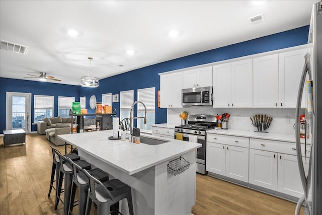 kitchen featuring sink, hanging light fixtures, hardwood / wood-style floors, white cabinets, and appliances with stainless steel finishes