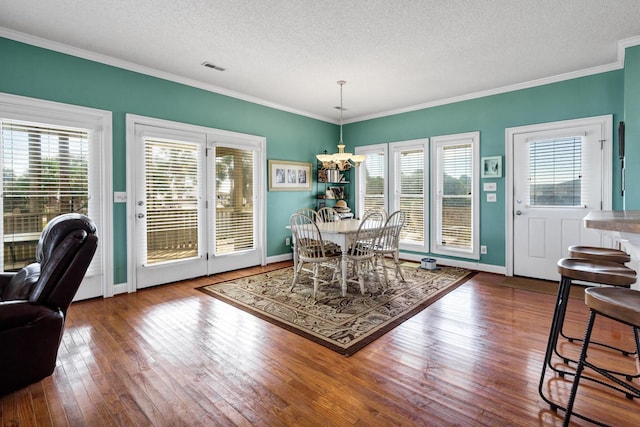 dining area featuring hardwood / wood-style floors, a notable chandelier, ornamental molding, and a textured ceiling