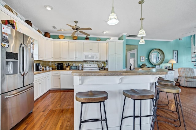 kitchen with hanging light fixtures, crown molding, wood-type flooring, white appliances, and white cabinets