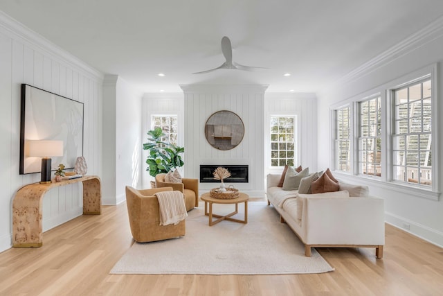 living room with crown molding, ceiling fan, a fireplace, and light wood-type flooring