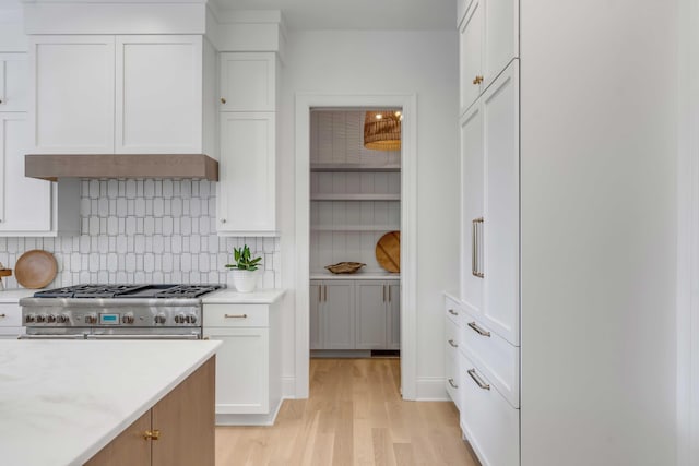 kitchen featuring light stone counters, double oven range, light hardwood / wood-style floors, decorative backsplash, and white cabinets