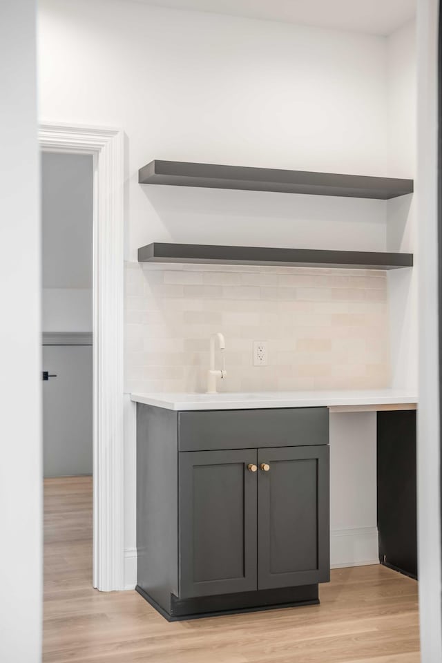 bar with gray cabinetry, sink, decorative backsplash, and light hardwood / wood-style flooring