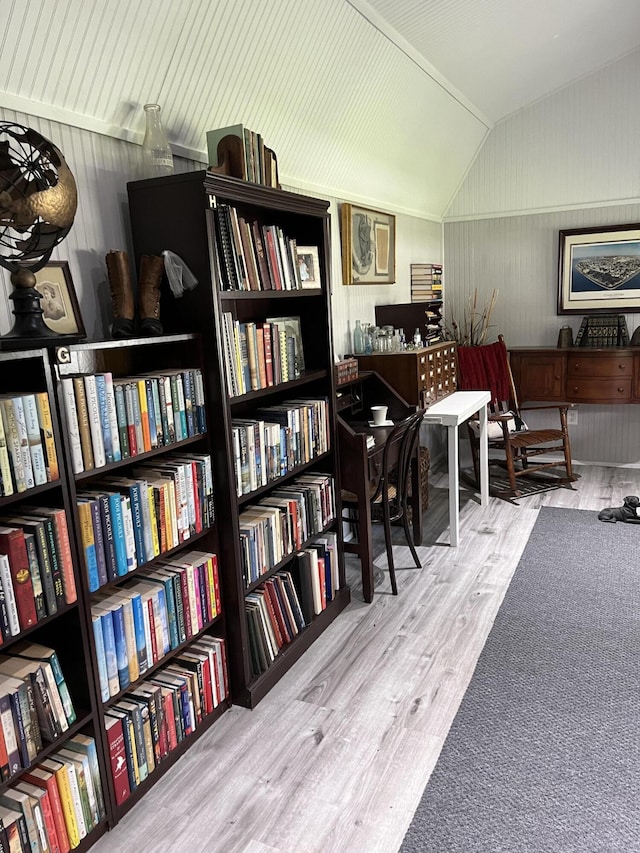 living area featuring vaulted ceiling, wall of books, and wood finished floors