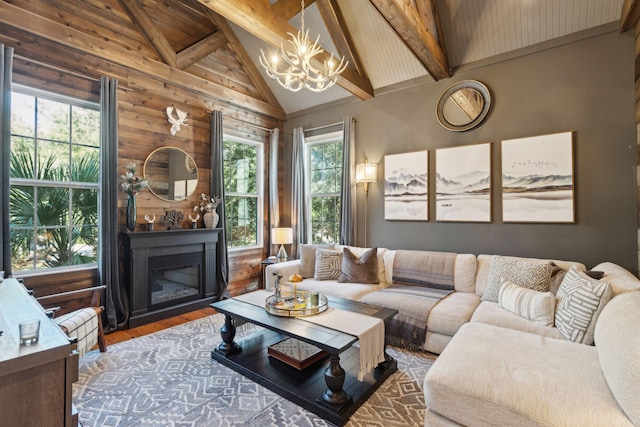 living room featuring wood-type flooring, beamed ceiling, a notable chandelier, high vaulted ceiling, and rustic walls