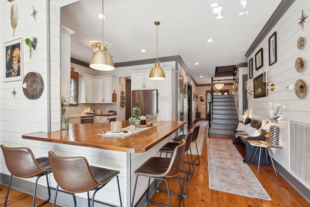 kitchen with stainless steel fridge with ice dispenser, hanging light fixtures, crown molding, white cabinets, and butcher block counters