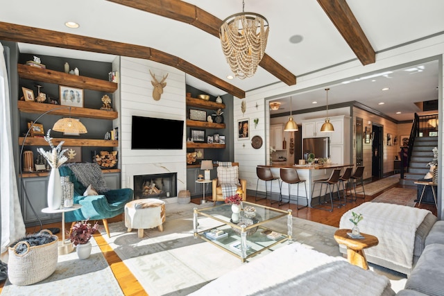 living room with an inviting chandelier, a fireplace, hardwood / wood-style floors, wood walls, and built in shelves