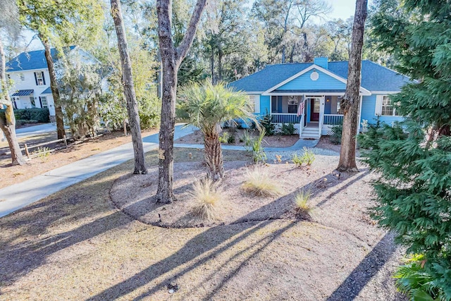 view of front of home featuring driveway, covered porch, a shingled roof, and a chimney