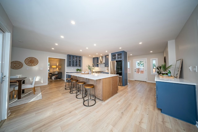 kitchen featuring a spacious island, light countertops, wall chimney exhaust hood, smart refrigerator, and glass insert cabinets