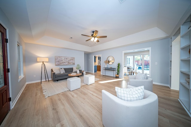 living room with a ceiling fan, a tray ceiling, baseboards, and wood finished floors