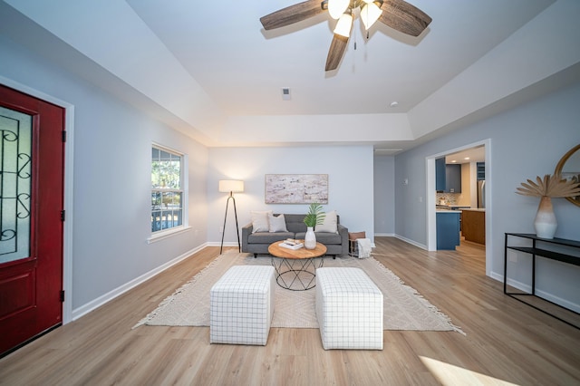 living area featuring a tray ceiling, baseboards, and light wood finished floors