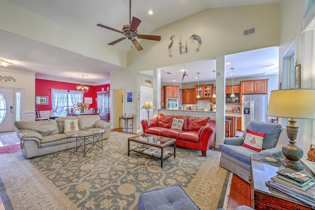 living area with high vaulted ceiling, ceiling fan with notable chandelier, wood finished floors, and visible vents