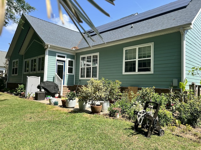 rear view of house with solar panels, roof with shingles, a lawn, central air condition unit, and entry steps