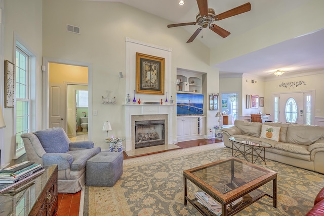 living area featuring a ceiling fan, visible vents, wood finished floors, high vaulted ceiling, and a fireplace with raised hearth