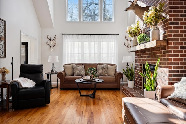 living room with a fireplace, light hardwood / wood-style flooring, a high ceiling, and plenty of natural light