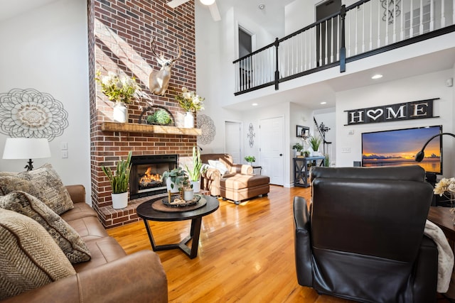 living room with hardwood / wood-style flooring, a fireplace, ceiling fan, and a high ceiling
