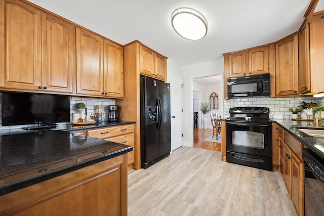 kitchen featuring dark stone countertops, backsplash, black appliances, and light hardwood / wood-style floors