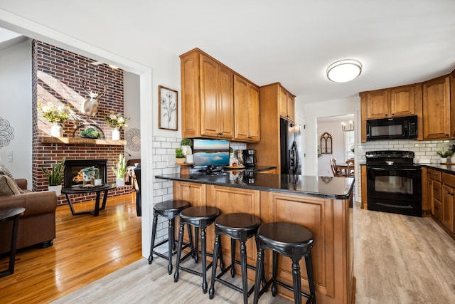 kitchen featuring light hardwood / wood-style flooring, backsplash, a fireplace, black appliances, and a kitchen bar