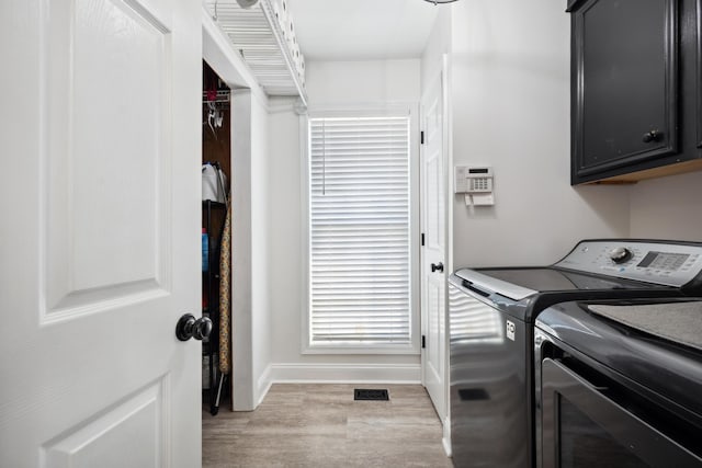 clothes washing area with washer and clothes dryer, cabinets, and light wood-type flooring