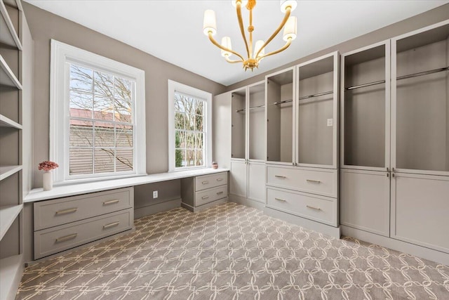 spacious closet featuring a notable chandelier and built in desk