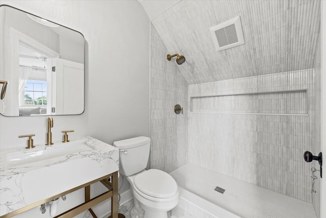 bathroom with tiled shower, lofted ceiling, toilet, and vanity