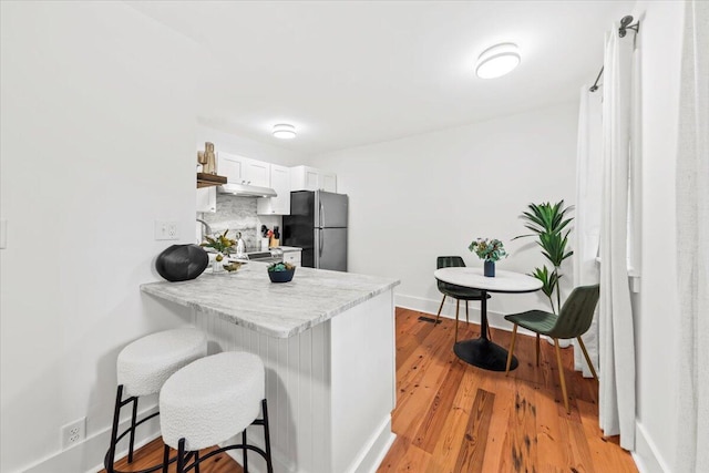 kitchen featuring white cabinetry, light wood-type flooring, stainless steel refrigerator, a kitchen breakfast bar, and decorative backsplash