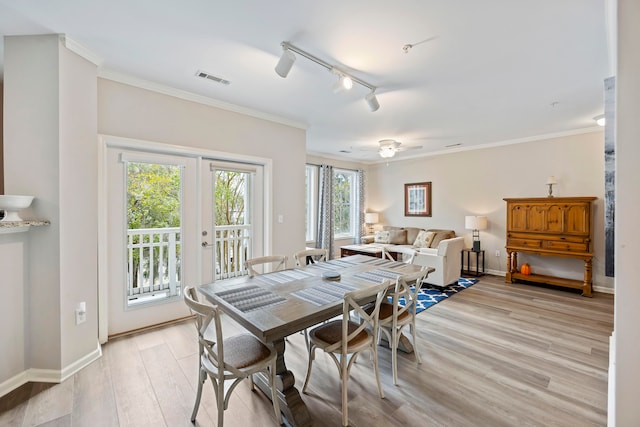 dining area featuring light wood-type flooring, rail lighting, a wealth of natural light, and ornamental molding