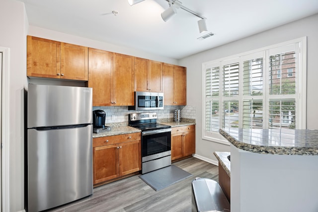 kitchen featuring light hardwood / wood-style flooring, backsplash, stainless steel appliances, light stone countertops, and kitchen peninsula