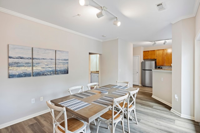 dining area with light wood-type flooring, crown molding, and track lighting