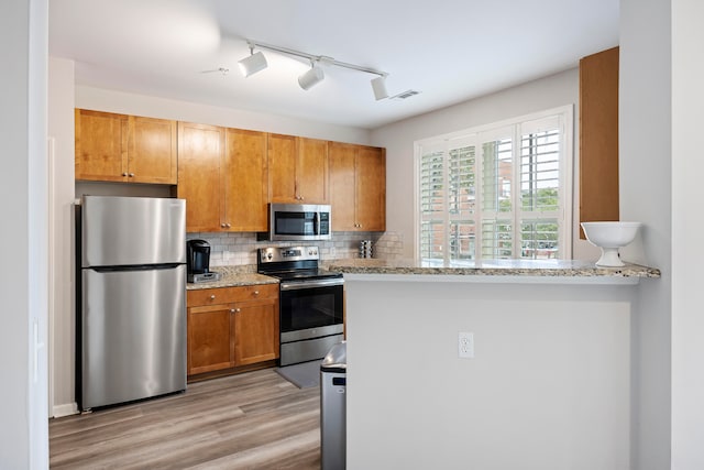 kitchen with appliances with stainless steel finishes, light stone countertops, kitchen peninsula, and backsplash