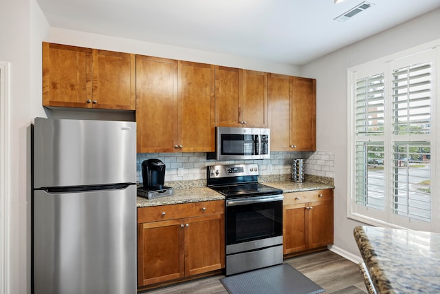 kitchen featuring hardwood / wood-style flooring, appliances with stainless steel finishes, backsplash, and light stone counters