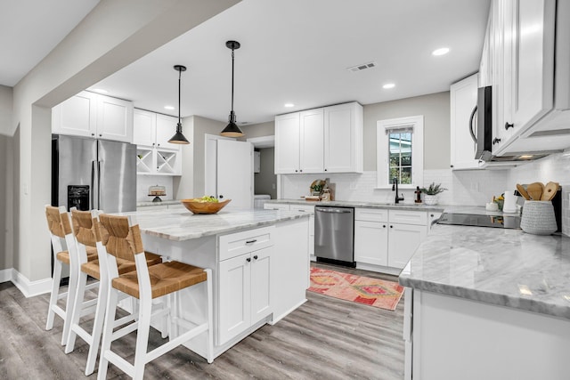 kitchen with hanging light fixtures, a kitchen island, white cabinets, and appliances with stainless steel finishes