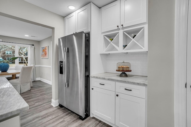 kitchen with stainless steel fridge with ice dispenser, backsplash, light stone countertops, and white cabinets