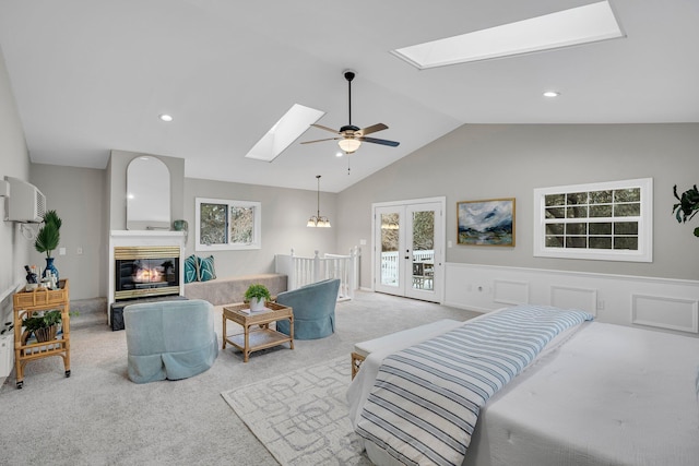 bedroom with ceiling fan, access to exterior, vaulted ceiling with skylight, and light carpet