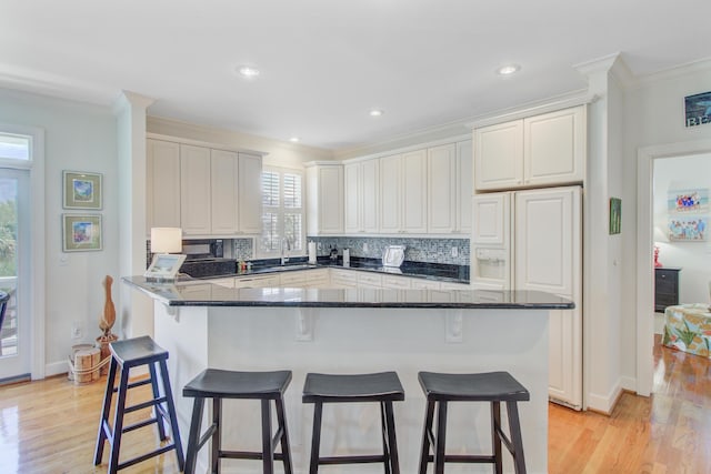 1647 Marsh Harbor Ln, Mount Pleasant, SC 29464 - kitchen with crown molding, a sink, a breakfast bar area, decorative backsplash, and light wood-type flooring
