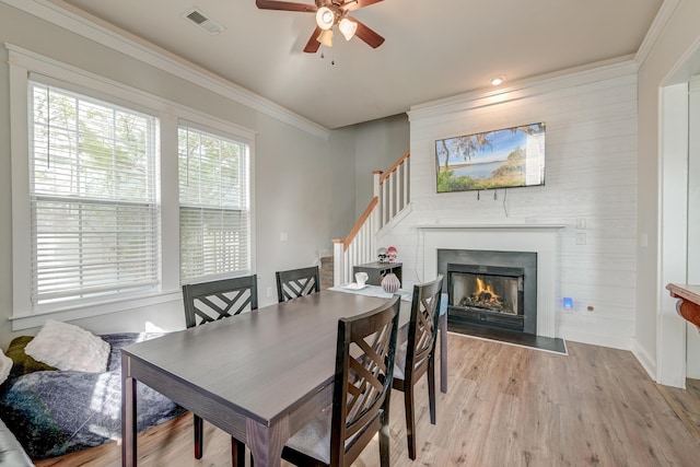 dining room with ceiling fan, crown molding, wooden walls, and light hardwood / wood-style flooring