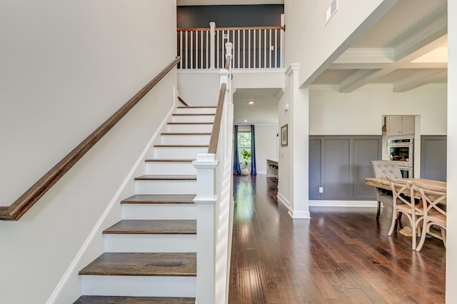 stairway featuring wood finished floors, a towering ceiling, crown molding, and beam ceiling